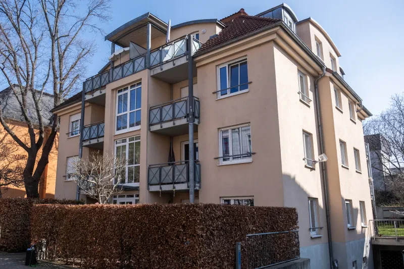Dresden, Klingenberger Straße 3. Ein vierstöckiges, rosafarbenes Wohnhaus hinter einer Hecke wird von der Sonne beschienen.