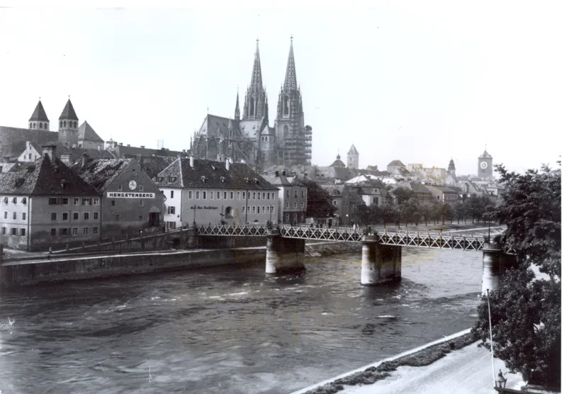 Über einem Fluss führt eine Brücke, dahinter Stadthäuser und ein Dom.