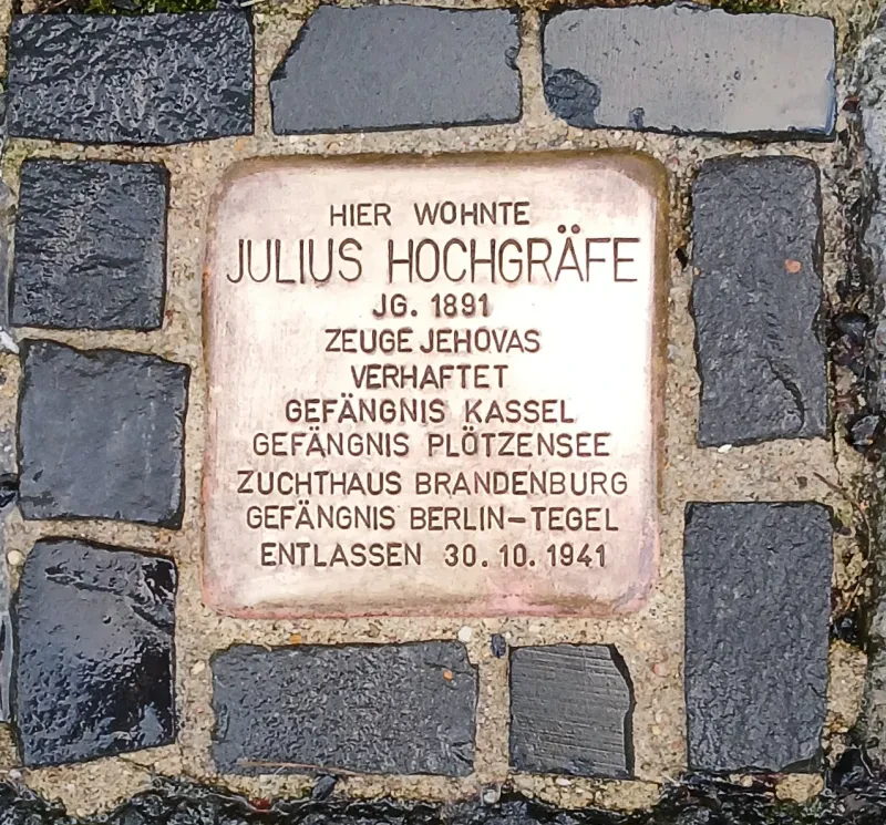 Stolperstein mit der Inschrift: „Hier wohnte Julius Hochgräfe Jg. 1891, Zeuge Jehovas, Verhaftet, Gefängnis Kassel, Gefängnis Plötzensee, Zuchthaus Brandenburg, Gefängnis Berlin-Tegel, Entlassen 30.10.1941“