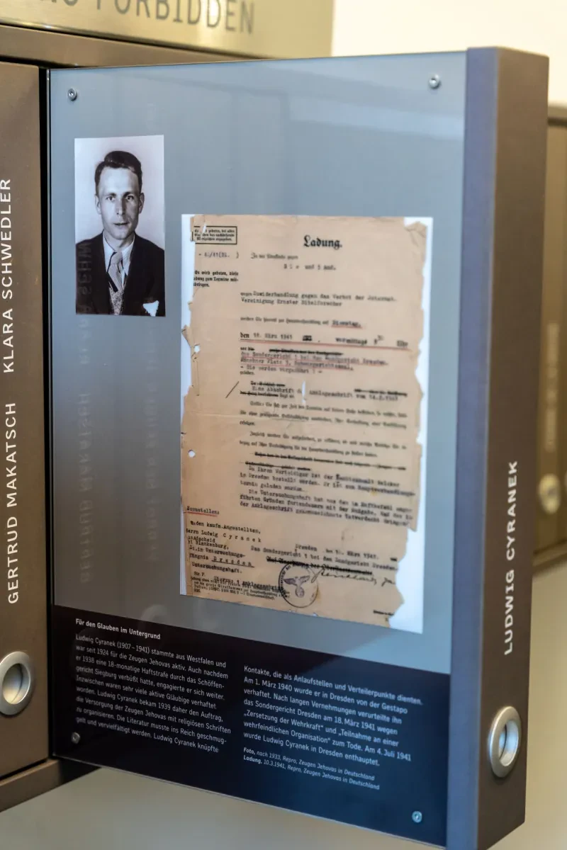 Einschubtafel mit dem Foto und der Ladung Ludwigs Cyraneks, sowie einem Begleittext zu seinen Aktivitäten als Zeuge Jehovas.