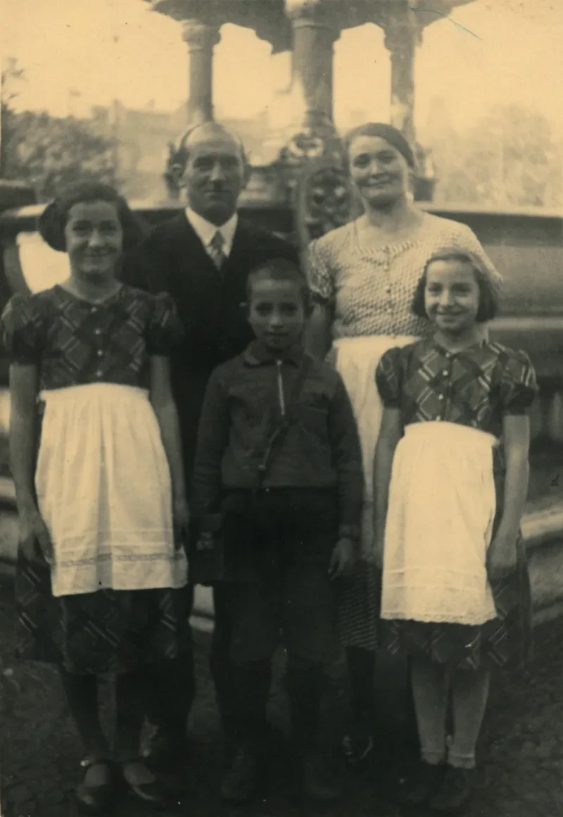 Eine Familie steht vor einem Springbrunnen?. Vater und Mutter und davor zwei Mädchen und ein junge (mitte). Sie sehen in die Kamera.