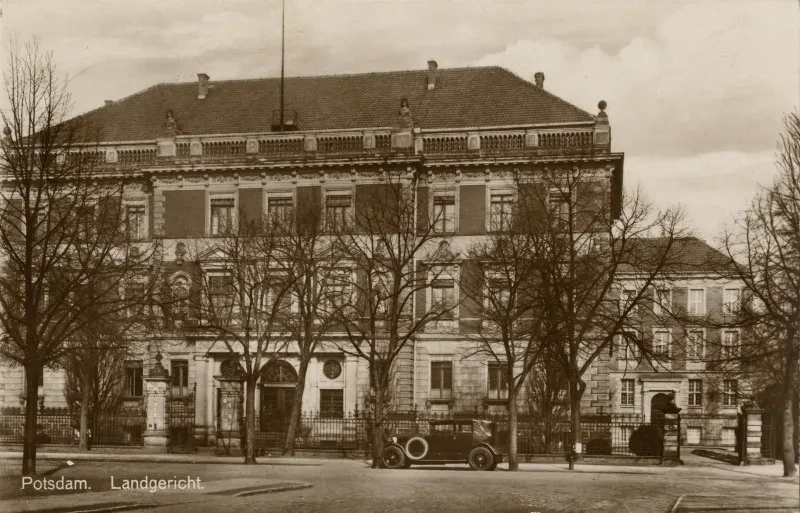 Ein dreistöckiges Gebäude hinter Bäumen, davor ein Auto. Die Postkarte trägt die Aufschrift "Potsdam. Landgericht"