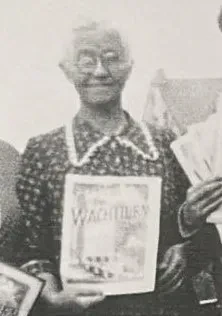 Eine ältere Dame mit Brille in einem Kleid hält die Zeitschrift "Der Wachtturm" in den Händen.