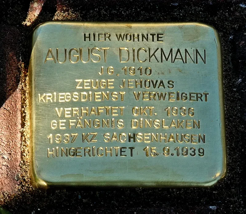 Stolperstein mit der Inschrift: "Hier wohnte August Dickmann / Jg. 1910 / Zeuge Jehovas / Kriegsdienst verweigert / Verhaftet Okt. 1936 / Gefängnis Dinslaken / 1937 KZ Sachsenhausen / Hingerichtet 15.9.1939"