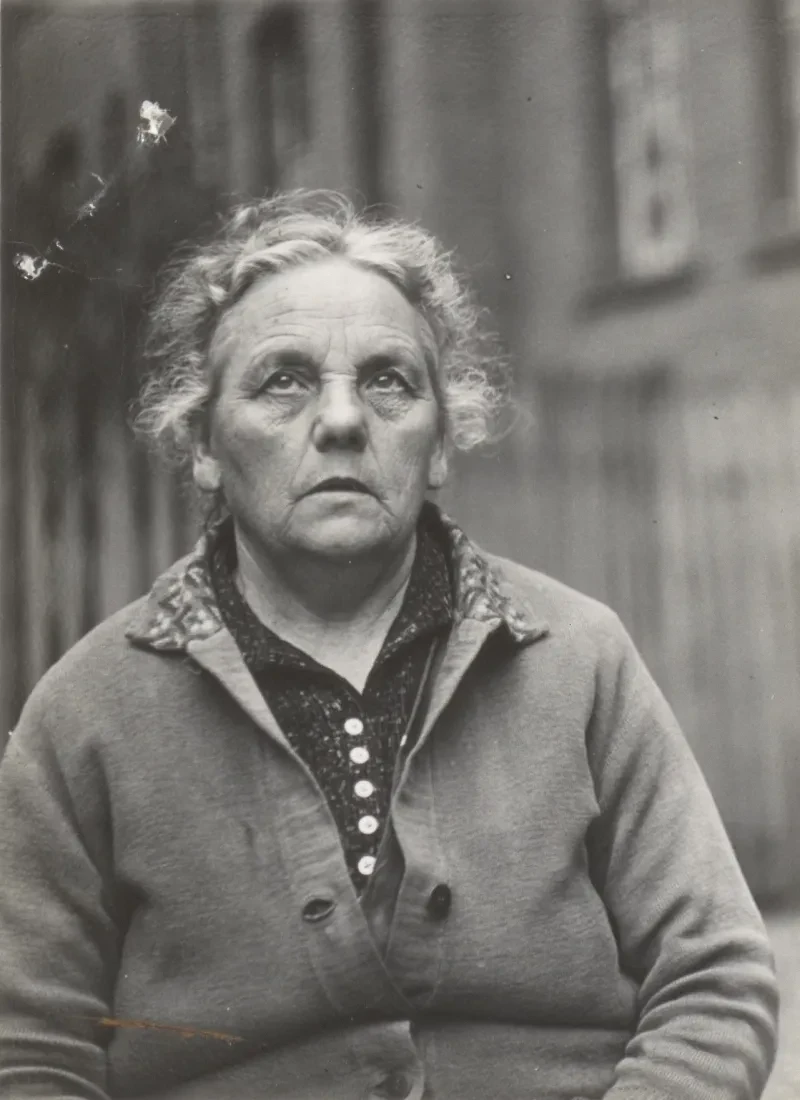 Eine ältere Frau in einer Strickjacke. Ihr Blick geht nach oben.