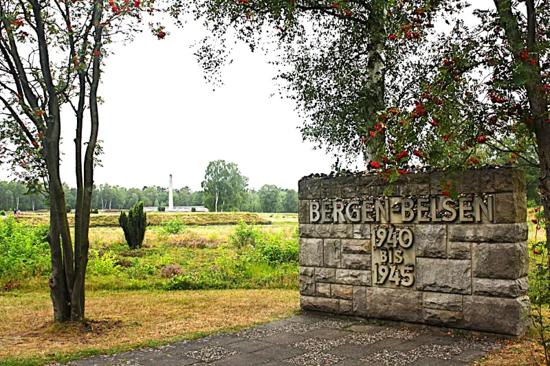 Auf einem freien Grüngelände steht eine Wand aus Natursteinen mit der Aufschrift "Bergen-Belsen 1940 bis 1945".