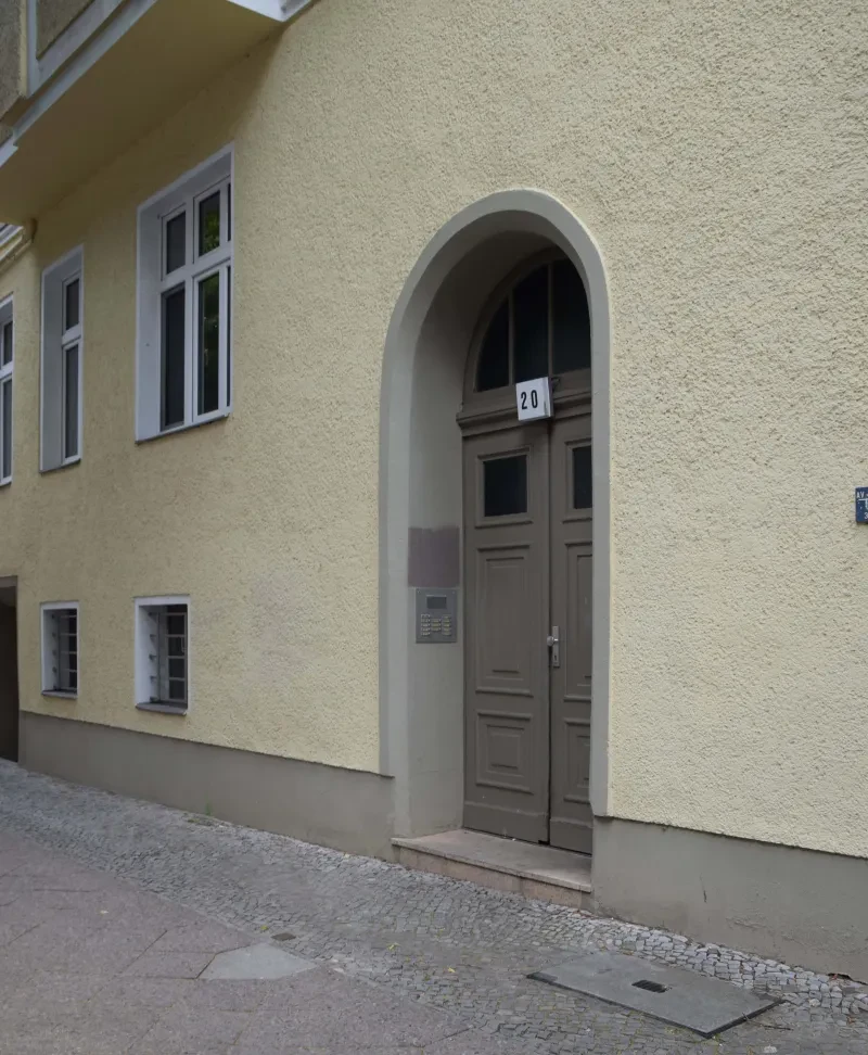 Ein Hauseingang. An der Eingangstür steht die Nr. 20. Vor dem Eingang liegt ein Stolperstein.