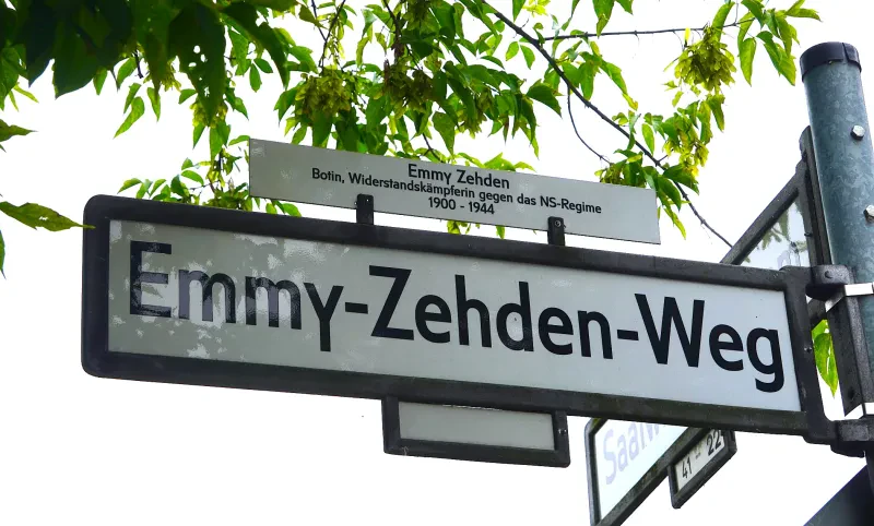 Über dem Straßenschild "Emmy-Zehden-Weg" hängt eine erklärende Zusatzinformation: "Emmy Zehden. Botin, Widerstandskämpferin gegen das NS-Regime, 1900 - 1944".