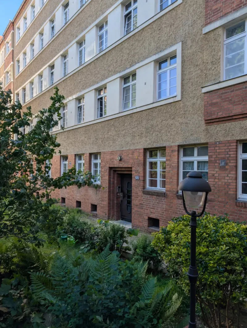 Ein langgestreckter fünfstöckiger Wohnblock hinter einem begrünten Hang.