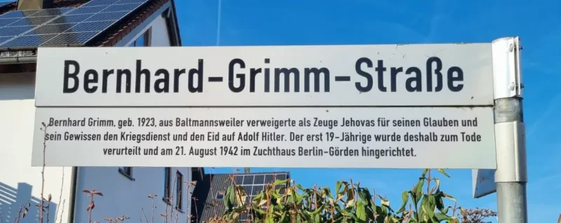 Straßenschild "Bernhard-Grimm-Straße" mit dem Zusatz "Bernhard Grimm, geboren 1923, aus Baltmannsweiler verweigerte als Zeuge Jehovas für seinen Glauben und sein Gewissen den Kriegsdienst und den Eid auf Adolf Hitler. Der erst 19-jährige wurde deshalb zum Tode verurteilt und am 21. August 1942 im Zuchthaus Berlin-Görden hingerichtet."