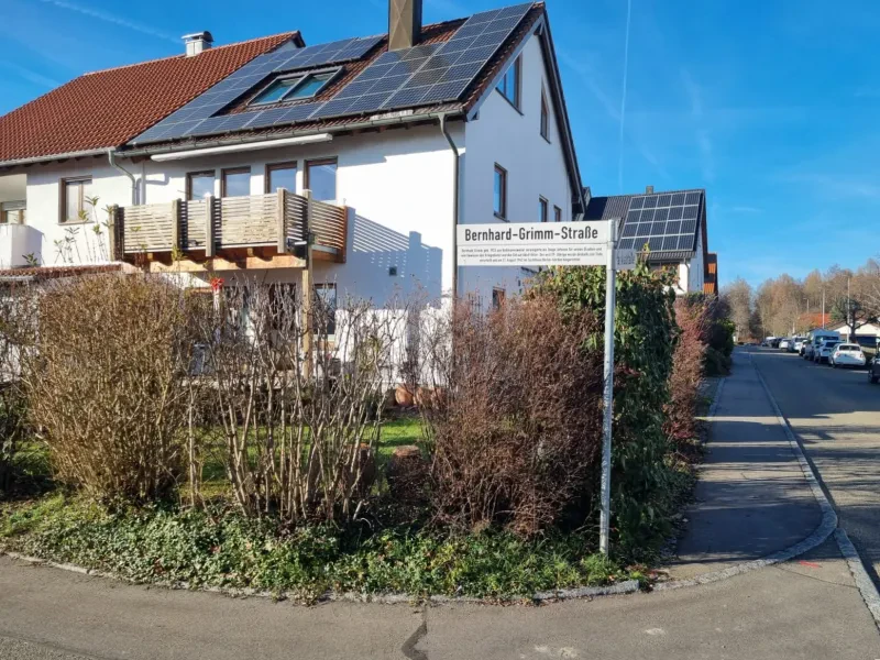 Straßenschild "Bernhard-Grimm-Straße" an einer Kreuzung eines Wohngebietes. Im Hintergrund stehen Häuser mit Sonnenkollektoren.