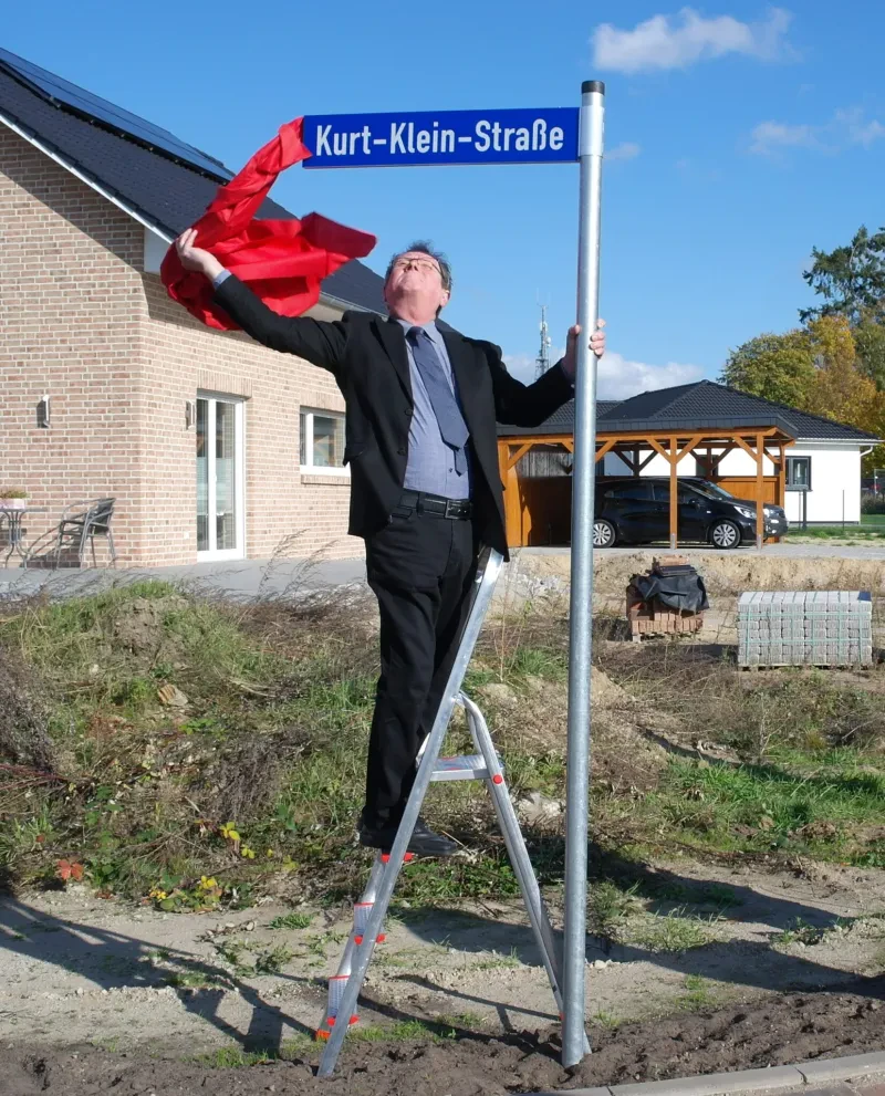 Uwe damm steht auf einer Leite und entfernt die Verhüllung des Straßenschildes.
