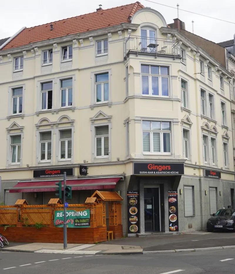 Ein über 100 Jahre altes weiißes, vierstöckiges Eckhaus an einer belebten Straße.
