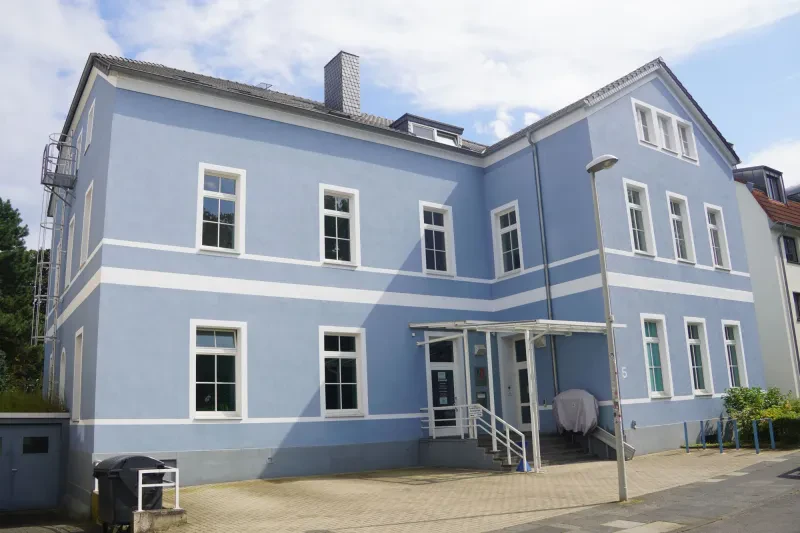 Ein zweistöckiges Gebäude mit winkelförmigem Grundriß und hellblauem Anstrich.