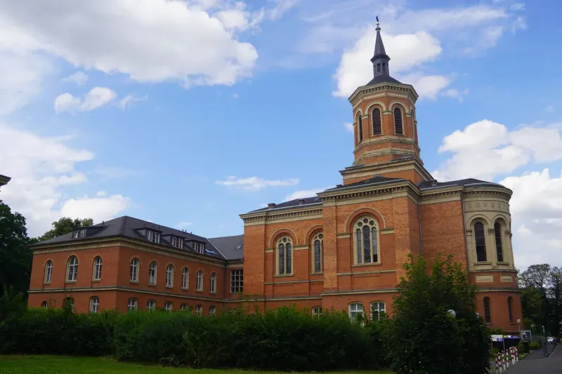Ein Klinikgebäude aus rotem Backstein ist mit einer Kapelle mit achteckigem Kirchturm verbunden.