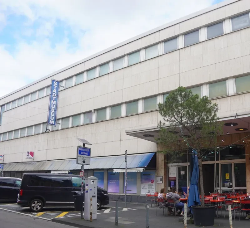 Ein älteres dreistöckiges Gebäude mit weißer Plattenfassade und einem Cafe im Erdgeschoss trägt den Schriftzug "Stadtmuseum".