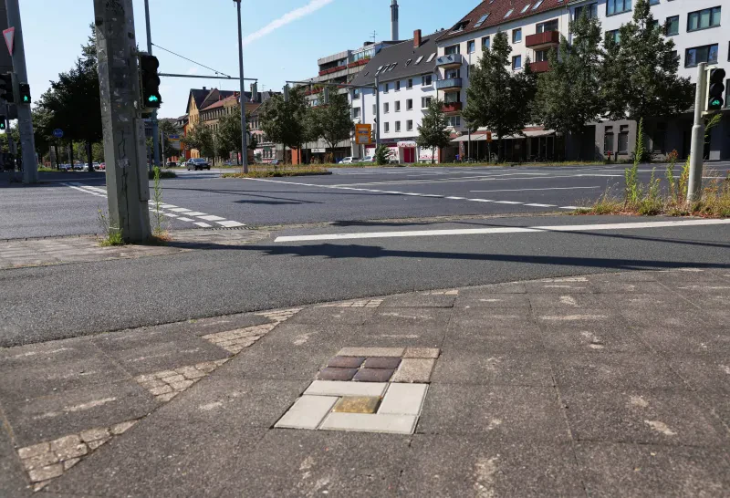 Eine Straßenkreuzung im Hintergrund, im Vordergrund sind fünf Stolpersteine im Pflaster zu sehen.