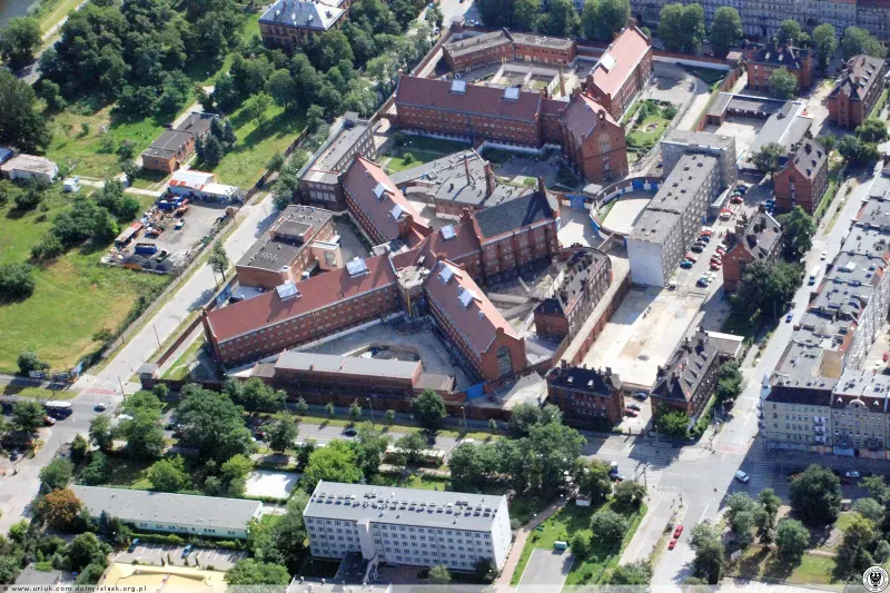 In der Luftaufnahme sieht man einen Gefängniskomplex, der von drei Seiten von Straßen umgeben ist. Der Männer und der Frauenbereich sind durch eine Mauer voneinander getrennt. Außerhalb der inneren Mauer befindet sich ein Parkplatz mit Verwaltungsgebäuden, die von einer weiteren Mauer umgeben sind.