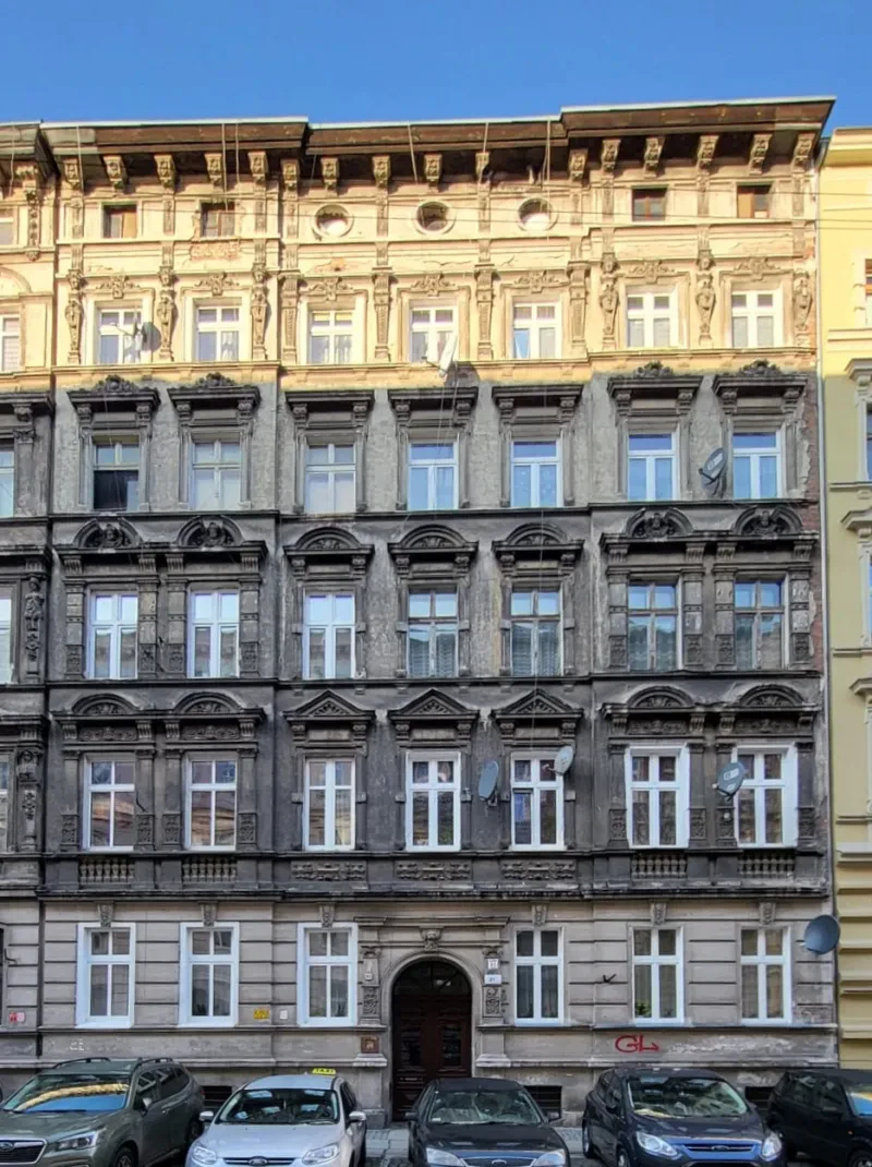 Ein graues, sechsstöckiges Steinhaus hat auf jedem Stockwerk sieben mit Stuck verzierte Fenster zur Vorderseite.