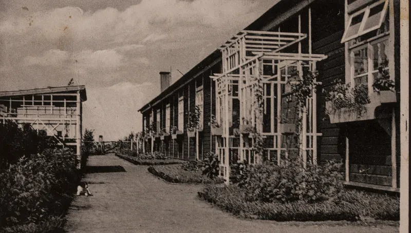 Vor dem Manschaftslager des Wachpersonals befinden sich gepflegte Gartenanlagen. An den Fenstern hängen Balkonkästen.