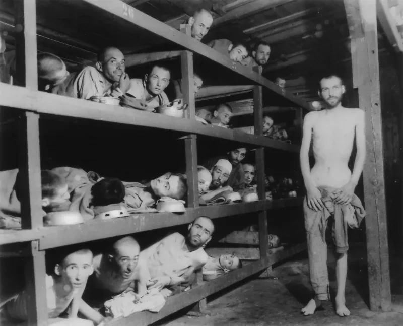 Ausgehungerte Häftlinge liegen in vierstöckigen Betten, ein Häftling steht, er ist halbnackt, man sieht den ausgemergelten Oberkörper. Die Blicke sind ernst, aber hoffnungsvoll.