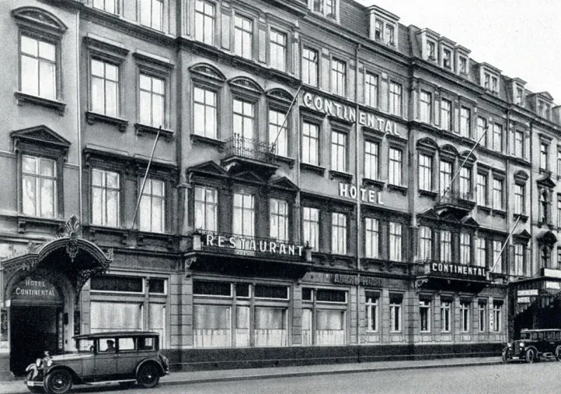 Ein 5-stöckiges Gebäude, davor parken zwei Autos. Die Inschriften "Continental Hotel" und "Restaurant Continental sind zu lesen.