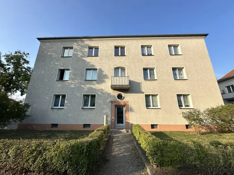 Ein helles dreistöckiges Wohngebäude mit Grünfläche vor dem Haus.