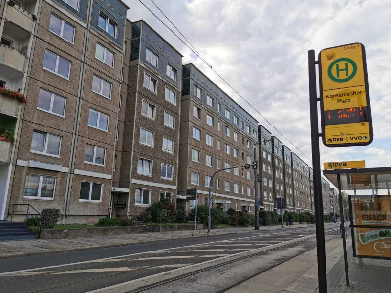 Eine Häuserfront mit sechsstöckigen Plattenbauten gegenüber einer Straßenbahnhaltestelle.