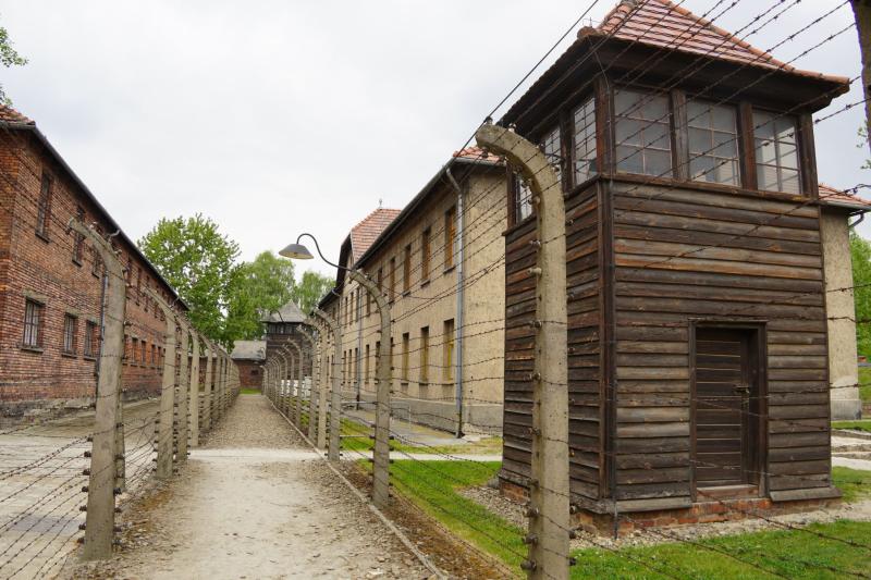 Auf der rechten Seite einer doppelten Zaunreihe, die Backsteingebäude von einander trennt, steht ein hölzerner Wachturm.