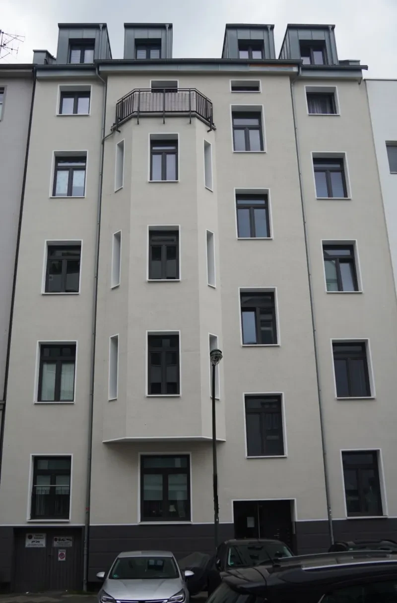 Ein schmales, hellverputztes, sechsstöckiges Wohnhaus mit aufgesetztem Giebel und ausgebautem Dachgeschoss.