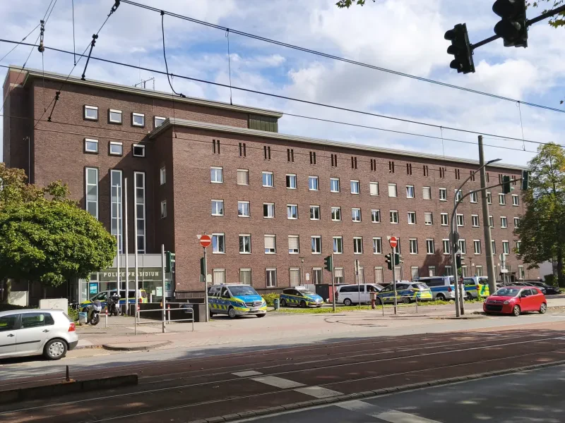 Ein mehrstöckiges Ziegelgebäude mit einigen Autos - vor allem Polizeiautos - davor. Über dem Eingang steht "Polizeipräsidium".
