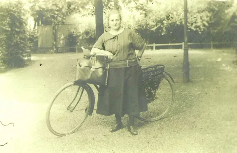 Eine junge Frau vor einem Fahrrad, an dessen Gepäckträger Werbung für die Zeitschrift "Das Goldene Zeitalter" gemacht wird.