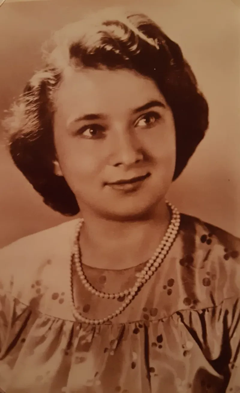 Portrait einer lächelnden, jungen Frau, die ein Kleid und eine Perlenkette trägt.