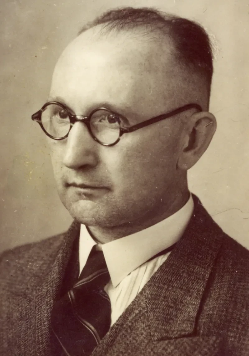 Ein Mann mit Sakko und Krawatte. Er trägt eine Brille.