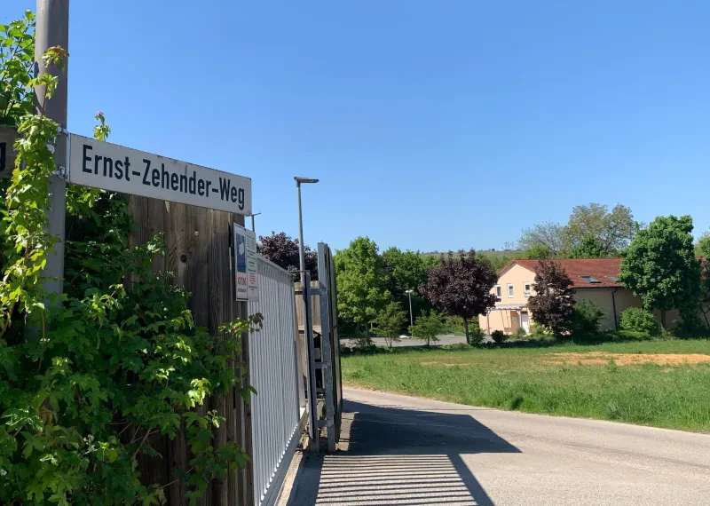 Das Straßenschild "Ernst-Zehender-Weg" sowie blick auf die Straße und eine Toreinfahrt.