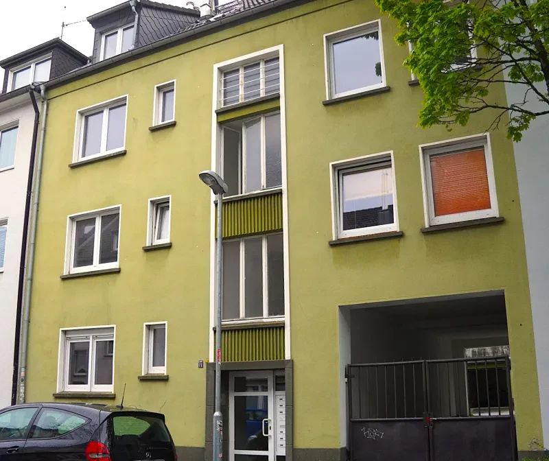 Ein vierstöckiges, gelb verputztes Wohnhaus mit ausgebautem Satteldach.