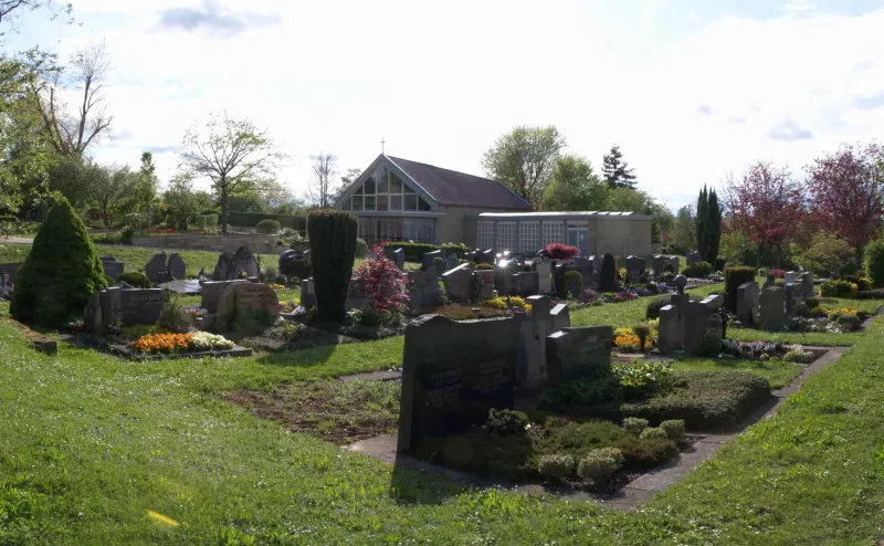 Ein Friedhof mit Grabsteinen, im Hintergrund eine Trauerhalle.