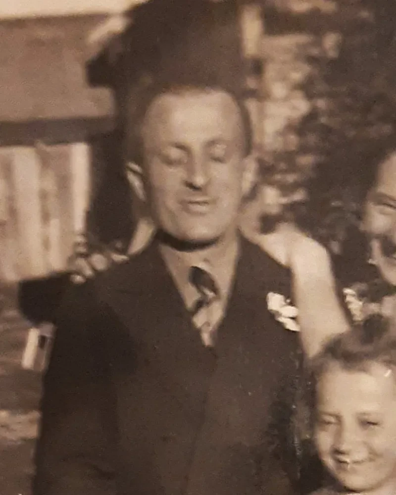 Ein Mann mit geschlossenen Augen, auf der Schulter die Hand seiner Frau.