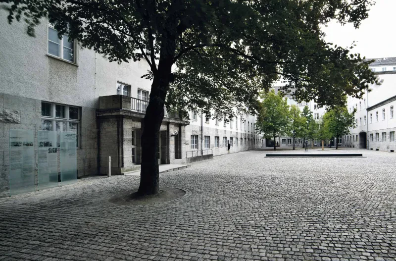 Ein gepflasterter Innenhof mit Bäumen und einem Denkmal.