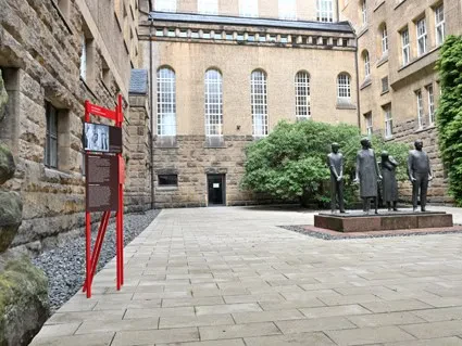 Eine Skulpturengruppe aus vier Personen steht im Innenhof eines Gerichtsgebäudes aus groben Steinen