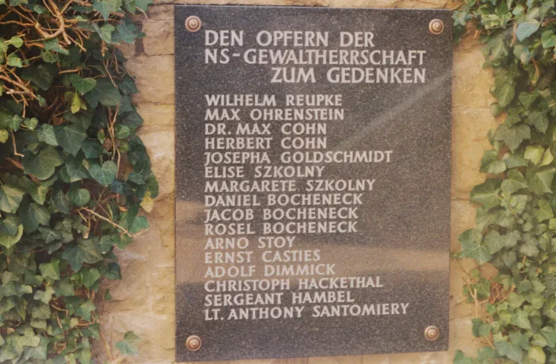 Eine Gedenktafel an einer Wand, rechts und links von Efeu umrankt.
