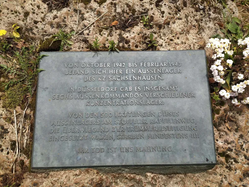Gedenktafel mit dem Text: "Von Oktober 1942 bis Februar 1943 befand sich hier ein Aussenlager des KZ Sachsenhausen. In Düsseldorf gab es insgesamt sechs Aussenkommandos verschiedener Konzentrationslager. Von den 500 Häftlingen dieses Aussenlagers am Stoffeler Kapellenweg, die überwiegend zur Trümmerbeseitigung eingesetzt waren, starben mindestens 111. Ihr Tod ist uns Mahnung"