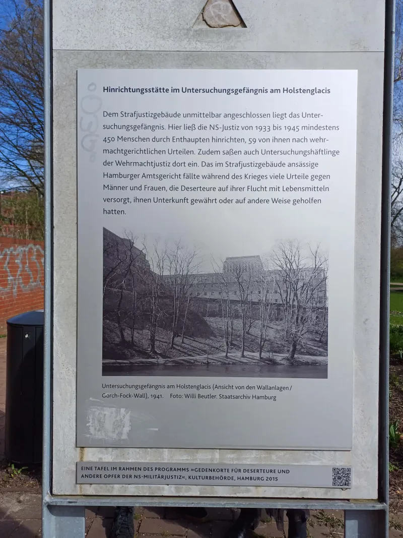 Gedenktafel zur Hinrichtungsstätte in der Hamburger Untersuchungsgefängnis am Holstenglacis in den Kleinen Wallanlagen, 2024. Text: Im Untersuchungsgefängnis am Holstenglacis befand sich eine Hinrichtungsstätte. Hier ließ die NS-Justiz von 1933 bis 1945 mindestens 450 Menschen durch Enthaupten hinrichten, 59 von ihnen nach wehrmachtsgerichtlichen Urteilen. Zudem saßen auch Untersuchungshäftlinge der Wehrmachtjustiz dort ein. Das im Strafjustizgebäude ansässige Hamburger Amtsgericht fällte während des Krieges viele Urteile gegen Männer und Frauen, die Deserteure auf ihrer Flucht mit Lebensmitteln versorgt, ihnen Unterkunft gewährt oder auf andere Weise geholfen hatten.