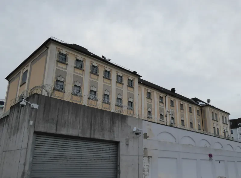 Ein Gefängnisgebäude, gelb gestrichen, hinter einer Mauer mit Stacheldraht.