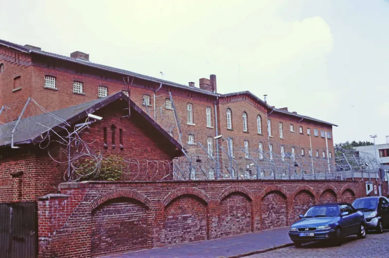 Ein Gefängnisgebäude hinter einer mauer mit Stacheldraht.