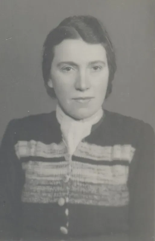 Eine Frau in den 40er Jahren mit Strickjacke schaut ernst in die Kamera.