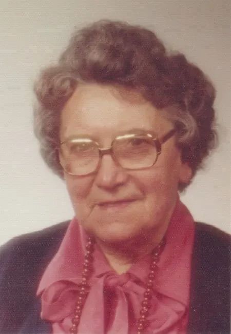 Eine ältere Dame mit roter Bluse und Brille schaut in die Kamera des Fotografen.