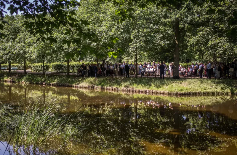 Ein Teich, im Hintergrund Bäume und eine Menschenmenge.