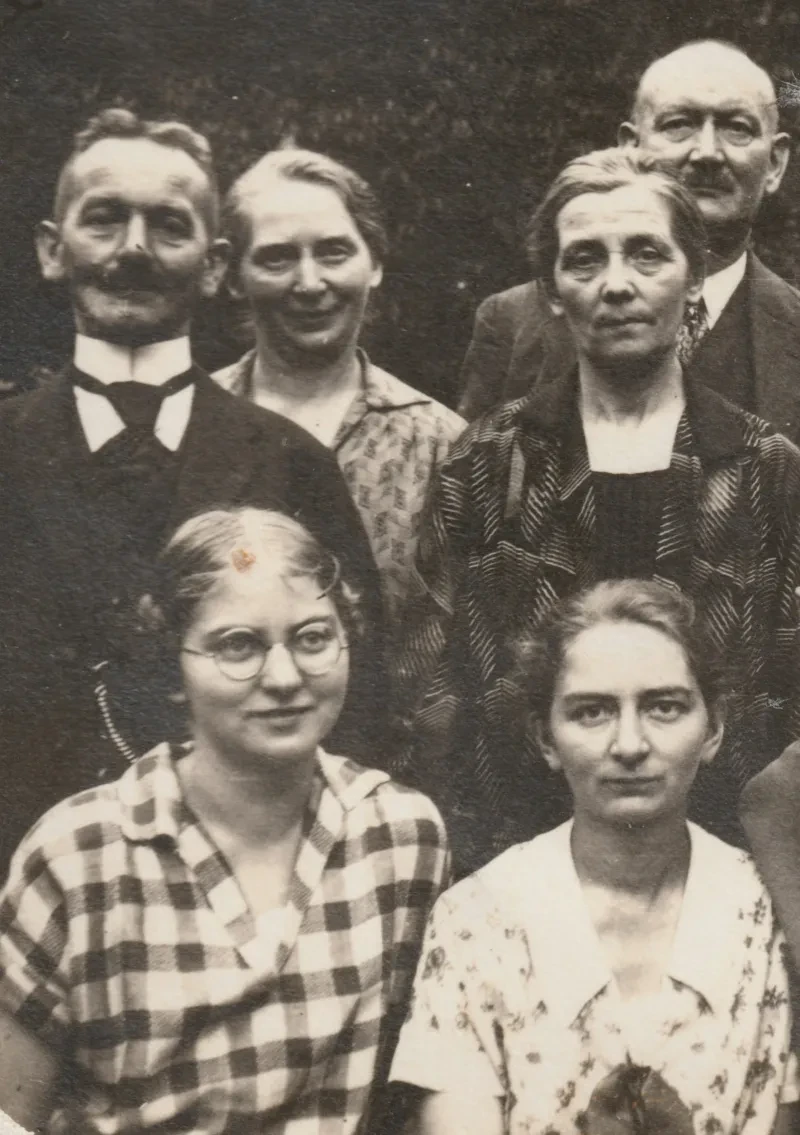 Zwei junge Frauen in Sommerkleidung sitzen vor zwei älteren Ehepaaren in festlicher Kleidung.
