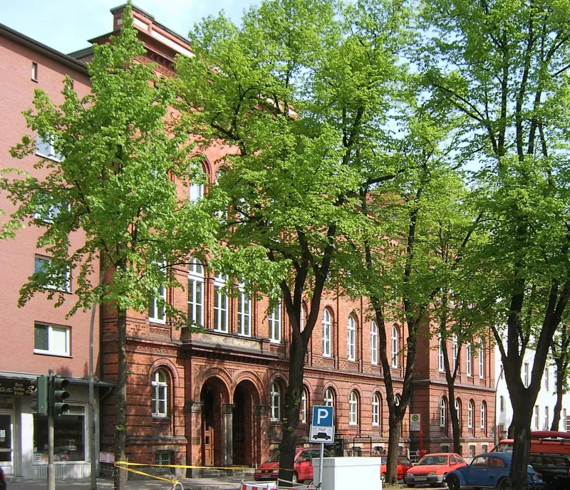 Ein roter Backsteinbau, davor parken Autos.